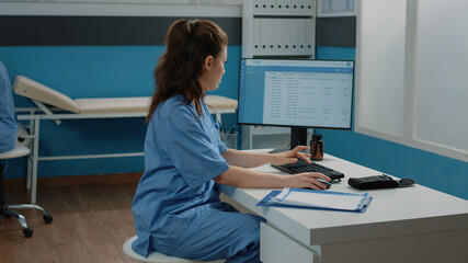 Woman working as nurse with computer and documents in cabinet, checking files for examination...
