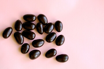Chocolate candy on pink background, dark chocolate covered almonds top view