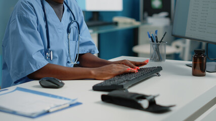 Close up of medical assistant typing on computer keyboard in cabinet for appointments with...