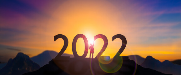 Silhouette businessman celebrating raising arms between word 2022 with sunset sky at Mountain and...
