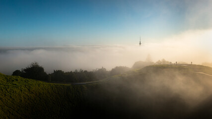 View from Mt Eden summit with fog drifting over volcanic crater and Sky Tower, Auckland city.
