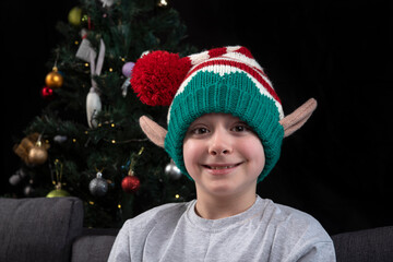 Portrait of boy wearing Christmas elf hat against the background of the Christmas tree