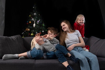 Naklejka premium Cozy family evening - mom and three happy smiling children against the background of the Christmas tree