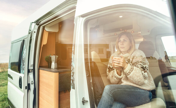 Woman with a cup of coffee sitting in the front seat of a camper van