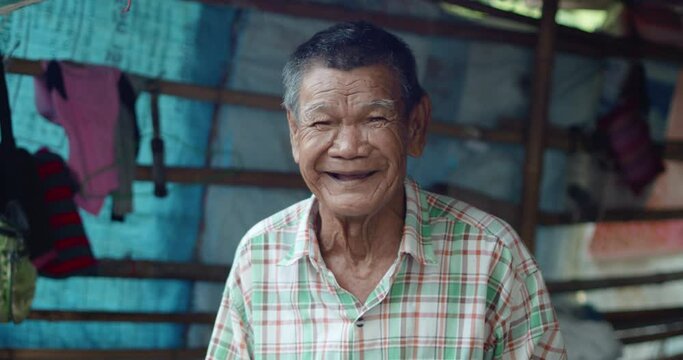 An Asian man who is more than seventy years old and works as a wage earner in a farm, live in a poor house, smiling and laughing happily in a countryside.