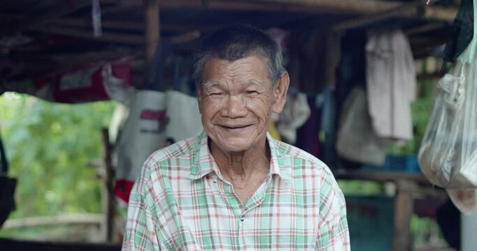 An Asian man who is more than seventy years old and works as a wage earner in a farm, live in a poor house, smiling and laughing happily in a countryside.