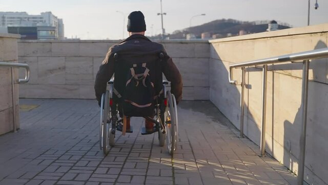 adult man in wheelchair is using handicapped ramp in modern city for moving