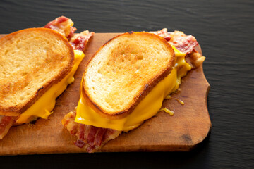Homemade Bacon Grilled Cheese Sandwich on a rustic wooden board on a black background, side view. Close-up.