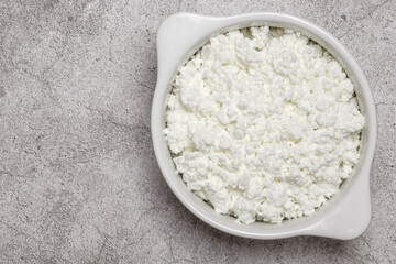 Fresh dairy farm product cottage cheese in ceramic bowl on a concrete background on table close-up top view. Healthy food containing calcium, lactose, protein, methionine, amino acid, vitamin, casein
