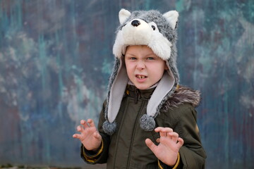 The roar of a wolf. Child in a wolf hat on gray background, outdoor.