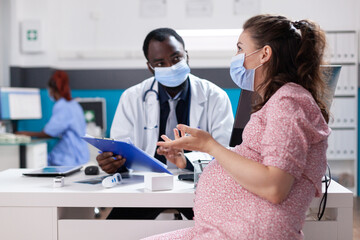 Fototapeta premium Woman expecting child and having discussion with physician about pregnancy and healthcare. General practitioner giving medical advice to pregnant patient during coronavirus pandemic