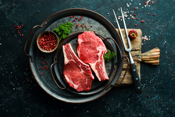 Beef fresh raw steak on the bone. On a black stone background. Organic food.