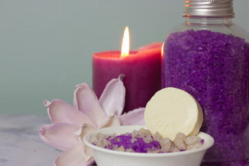 Obraz na płótnie Canvas A jar of purple lavender sea salt, bowl with a round bar of soap, burning lilac candle, beautiful flower composition. Spa treatment, body and facial care. Cosmetic products. Women's beauty. Copy space