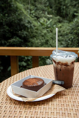 Close up of a plastic of Iced Cocoa cool drink and chocolate cake on table.