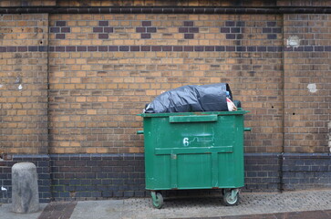 Green plastic mobile dumpster at the brick wall