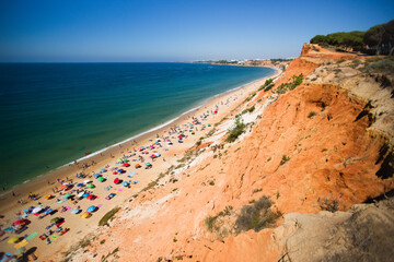 Orange cliff ending in the blue sea with tourists enjoying sun in 