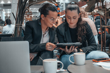 Mujeres empresarias trabajando en equipo escribiendo ideas y planteamientos en su tablet junto con su ordenador laptop en una cafeteria para terminar su trabajo