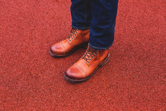 A man stands on the road in brown handmade leather boots. Men's stylish shoes for your ad with space for text