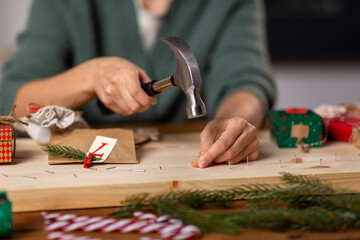 Obraz premium winter holidays and hobby concept - close up of woman with hammer hammering nails in wooden board and making advent calendar at home