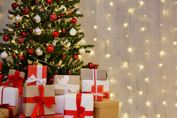 decorated Christmas tree, heap of gift boxes and copy space over grey wall with festive led lights