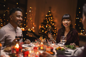 holidays, party and celebration concept - happy friends having christmas dinner at home and drinking wine