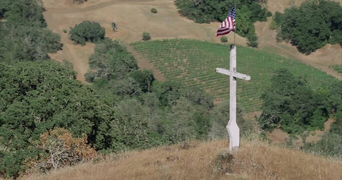 aerial of Wooden cross with american flag waving from it on top of a hill