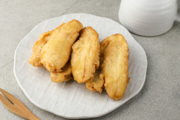Pisang goreng or banana fritters (deep fried banana fritter with flour batter), served in white plate on grey background. Selective focus image. Close up.
