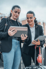 Mujeres empresaria de cabello oscuro formales con una sonrisa de pie revisando sus apuntes con contratos en la tableta digital en el centro de la ciudad caminando por la calle para llegar a su trabajo