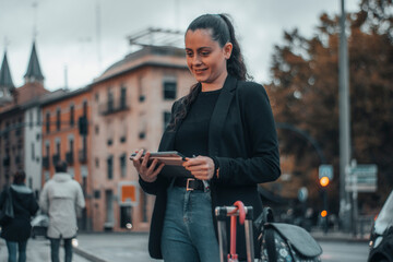 Fototapeta na wymiar Chica de cabello oscuro formal alegre y de pie sujetando su tablet digital en el centro de la ciudad caminando por la calle para llegar a su trabajo