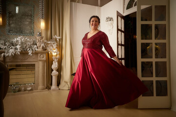 A beautiful majestic solemn fat queen in a red elegant dress in a beautiful hall in the palace. A chubby model poses during a photo shoot