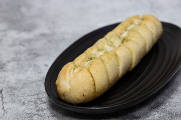 Cheesy garlic bread baton baguette with herbs on a black granite plate.  On a concrete background