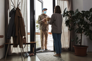 health protection, safety and pandemic concept - delivery man in face protective mask with parcel box and female customer at home