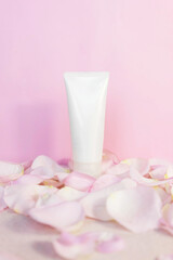 Cosmetic tube with face or body cream on a pink background with rose petals. Anti aging face care concept, vertical