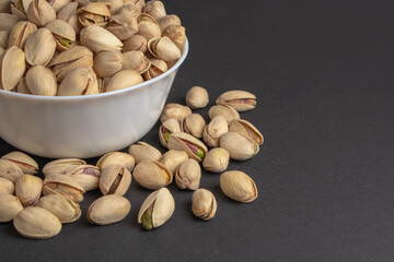 White bowl of pistachios on dark background