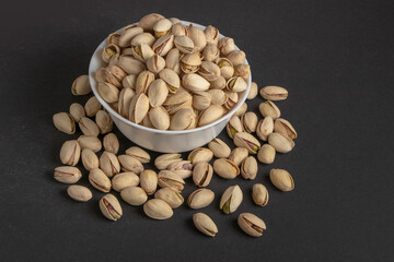 White bowl of pistachios on dark background