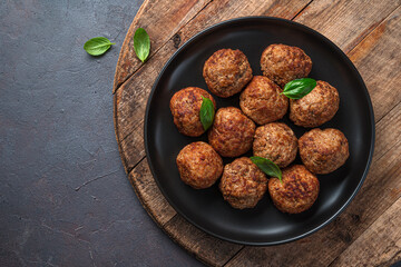 Meat meatballs in a black plate on a wooden board.
