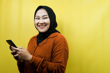 Beautiful young asian muslim woman with hands holding smartphone, smiling confident, enthusiastic and cheerful, view looking at empty space presenting something, isolated, advertising concept