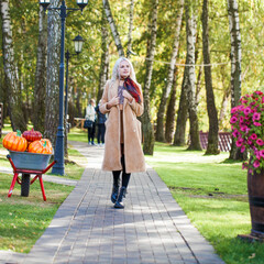 Fototapeta premium Young blonde girl in a beige coat walks in the autumn park