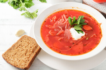 red borscht with sour cream and herbs in a white plate,  bread on a white  table