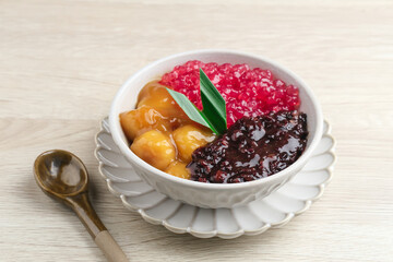Indonesian traditional dessert. Black glutinous rice with Candil and Sagu (Mutiara) porridge and pandan leaf. Served in a white bowl on wooden table. Blurred background and selective focus.
