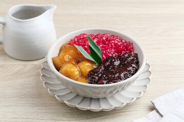 Indonesian traditional dessert. Black glutinous rice with Candil and Sagu (Mutiara) porridge and pandan leaf. Served in a white bowl on wooden table. Blurred background and selective focus.
