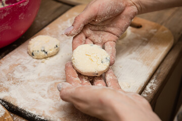 Woman hands prepare traditional slavic Cottage cheese pancakes (syrniki) for cooking on wooden board with flour