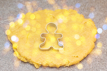 Form for cutting gingerbread men on raw rolled dough on a gray background with a golden round bokeh. Christmas food tradition