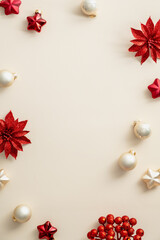 Minimal Christmas composition. Red and beige Xmas balls, stars, flowers on beige table. Elegant Vertical Christmas background. Flat lay, top view, copy space