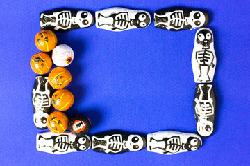 Obraz premium Creative frame of black and white skeleton candies and orange jack o lantern pumpkins with space for text on blue background. Halloween celebration concept. Invitation to a party on October 31st