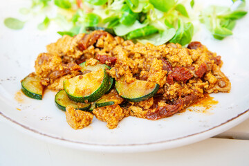 Vegan breakfast prepared with scrambled tofu and eggs, cooked with dried tomatoes and zucchini served with fresh lettuce and cucumber in white ceramic vintage plate