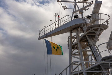 Low angle shot of the flag of Saint Vincent and the Grenadines waving in the wind on the ship's mast. Blue cloudy sky as a background