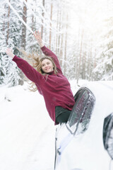 Fototapeta na wymiar white young blonde woman in a red sweater leaned out of the car window on a winter road in the woods