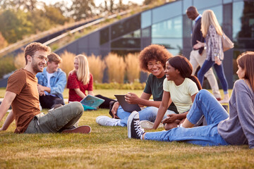 Group Of University Or College Students Sit On Grass Outdoors On Campus Talking And Working