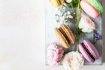 Various types of colorful macarons or macaroons decorated with flowers on light background. Traditional french almond dessert with sweet filling. Top view.